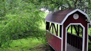 A small covered bridge with a red and white exterior, surrounded by lush greenery. - Hershey RV & Camping Resort (Lebanon)