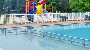 A swimming pool with a white fence, lounge chairs, and a children's play structure. - Hershey RV & Camping Resort (Lebanon)