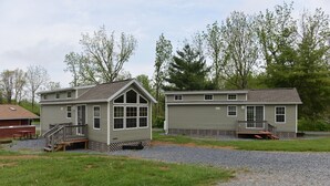 Two small, single-story cabins with attached porches, surrounded by a gravel driveway and grassy areas. - Hershey RV & Camping Resort (Lebanon)