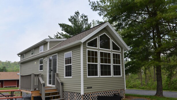 A small, single-story cabin with a front porch and a staircase leading to a deck. - Hershey RV & Camping Resort (Lebanon)