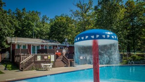 Une piscine agrémentée d’une fontaine, un espace de repos couvert et un bâtiment à la façade rouge.