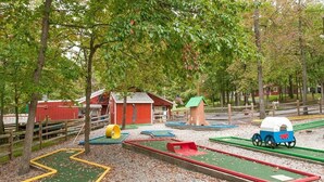 Un terrain de jeux avec une grange rouge, une petite maison et un chariot couvert.