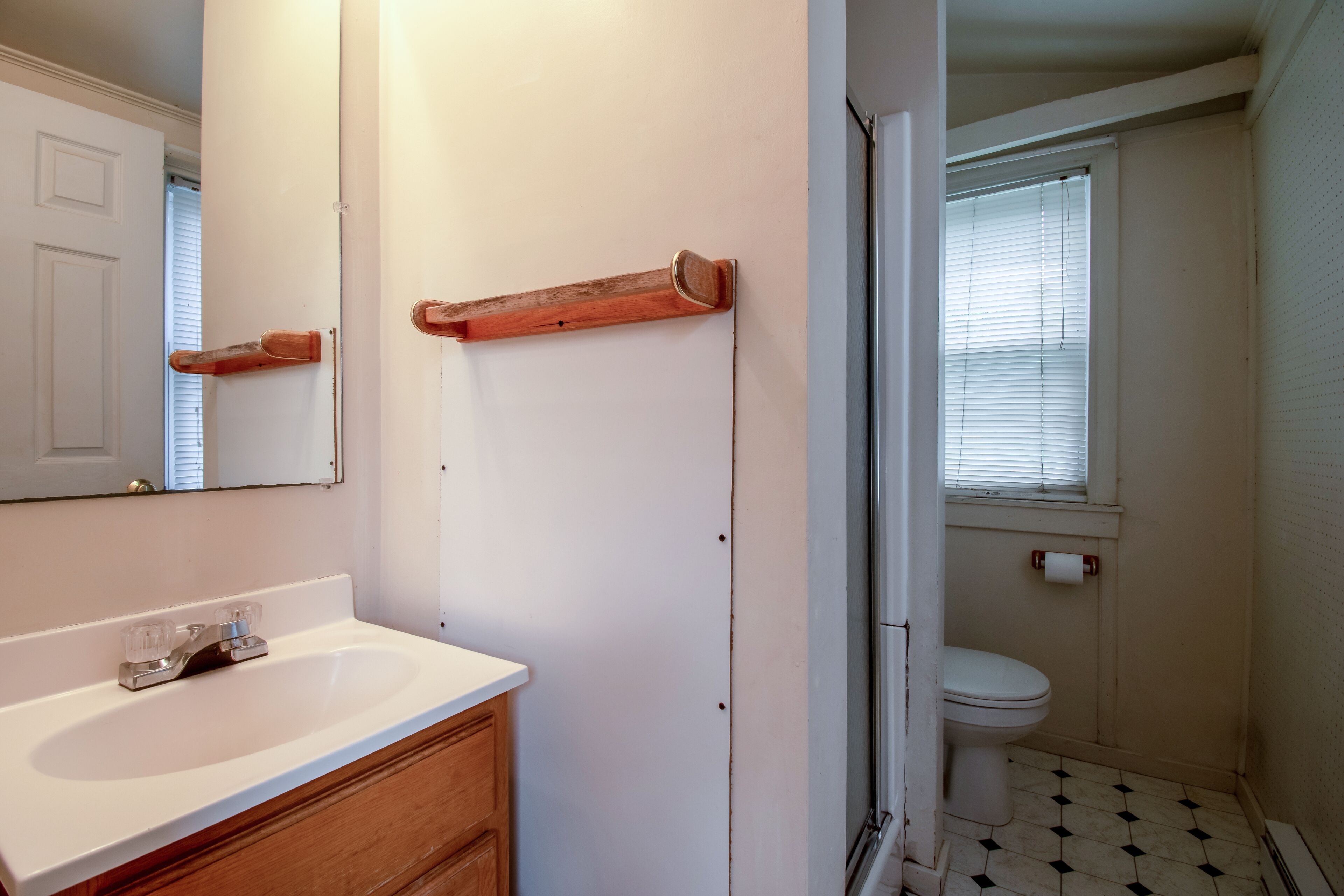 A bathroom with a white sink, wooden vanity, a mirror, a toilet, and a shower area.