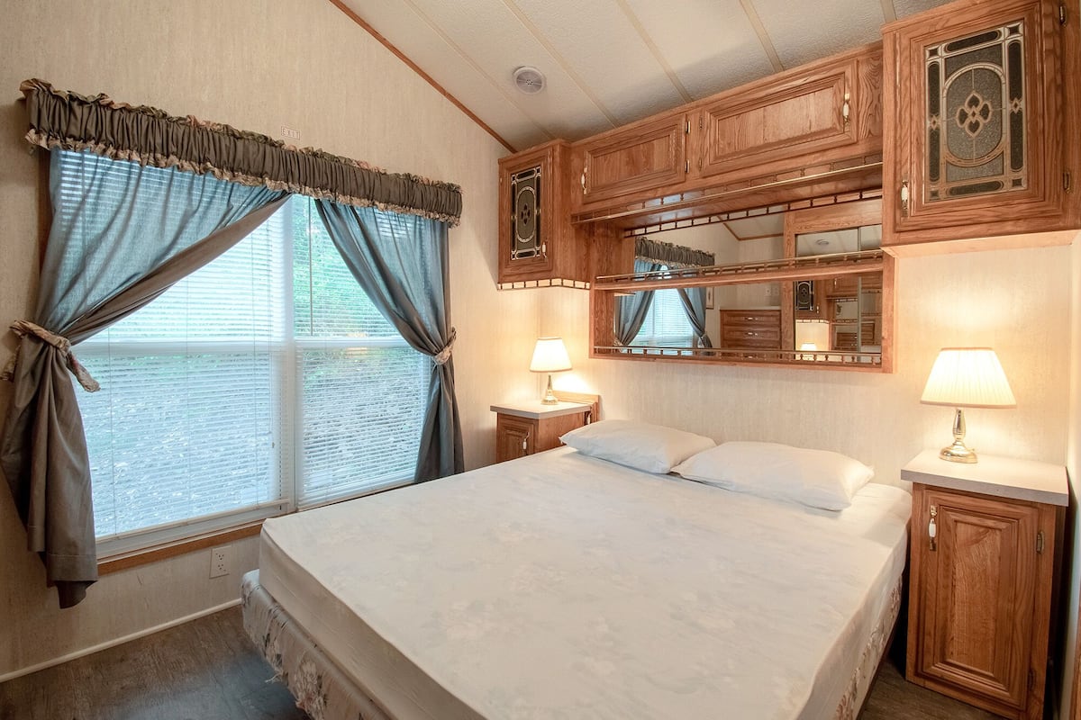 A bedroom with a large bed, two bedside tables with lamps, a mirror above the bed, and wooden cabinetry.