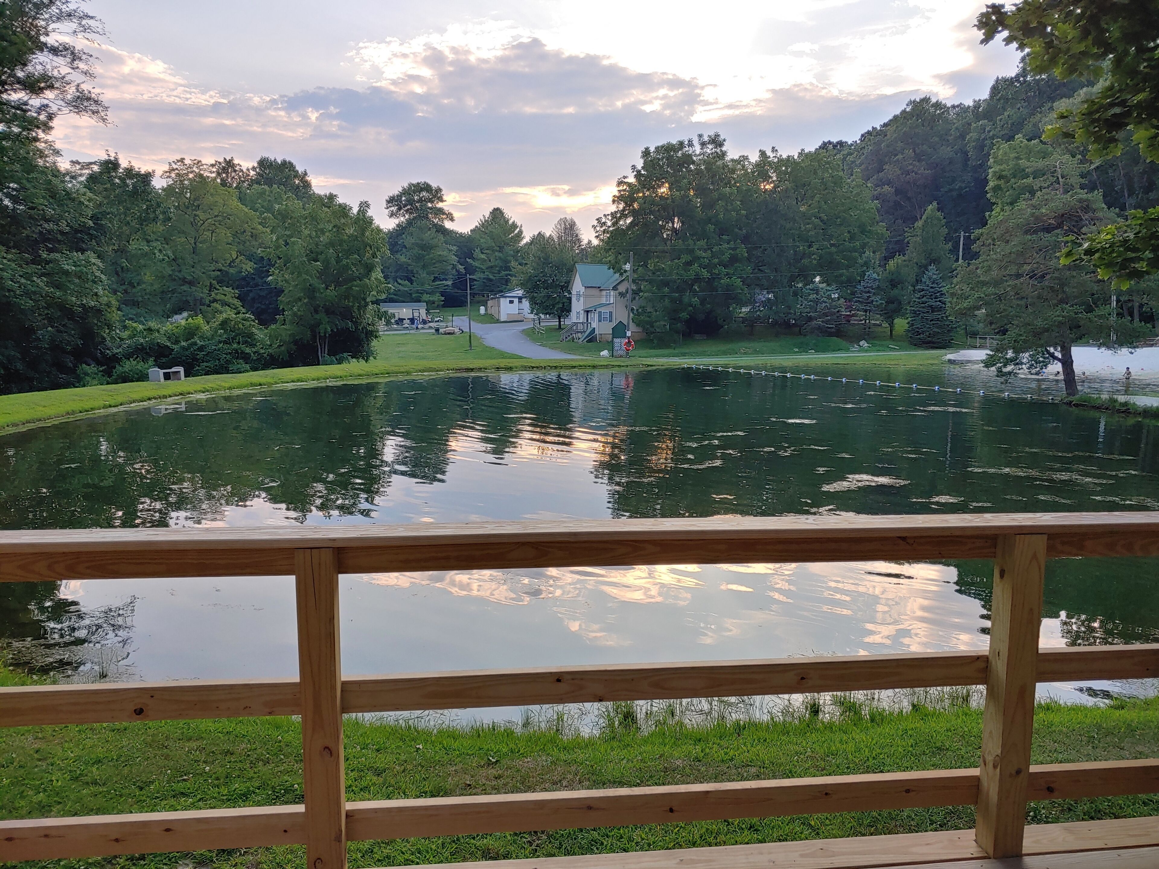 A wooden deck overlooking a pond with a pathway leading to a building surrounded by trees.