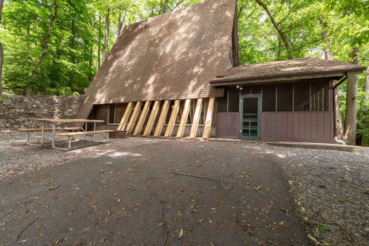 A rustic building with a sloped roof, a stone wall, and a wooden bench area.