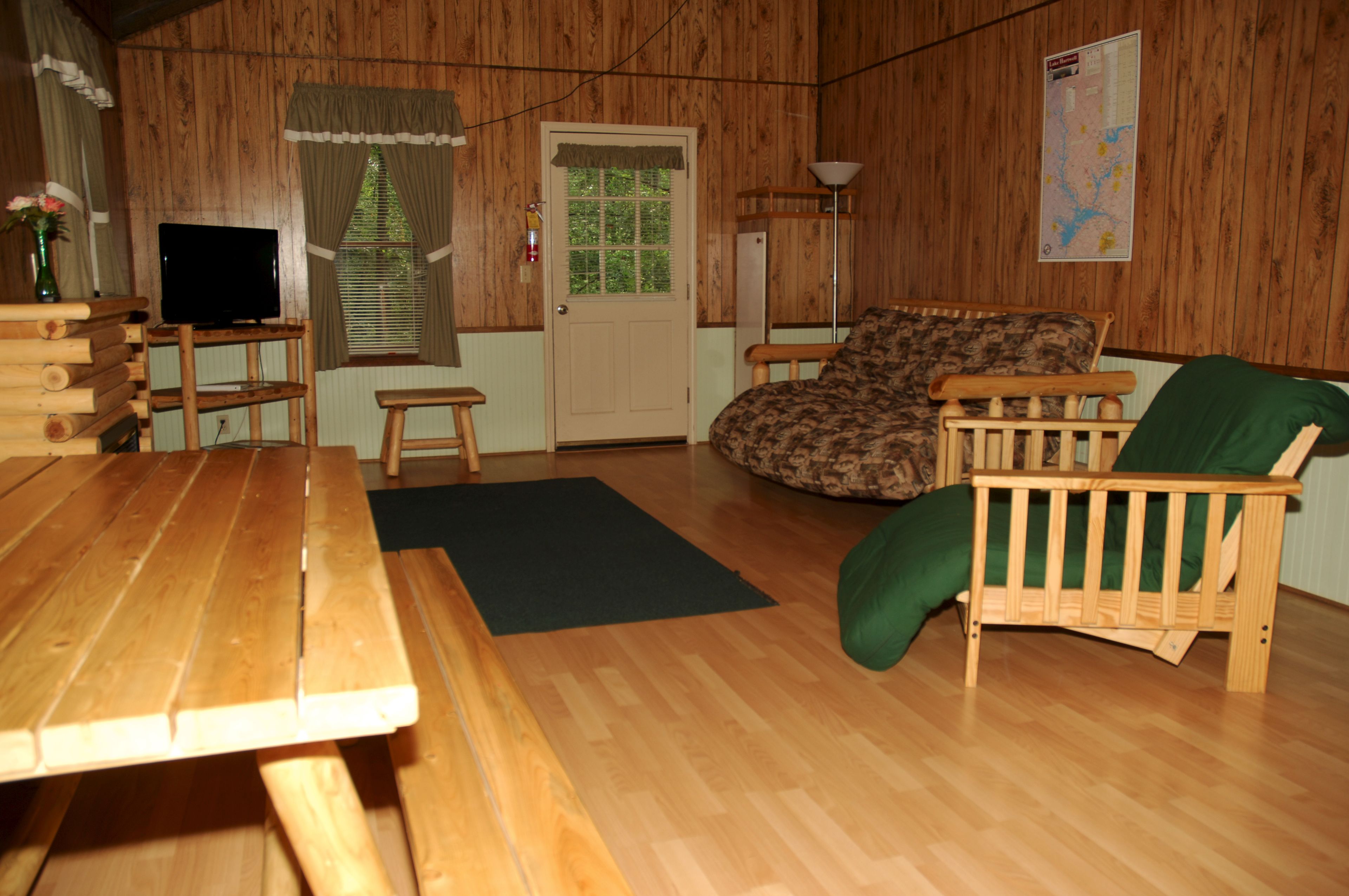 A wooden interior with a wooden table, a bench, a green cushion, a television on a stand, and a door with a window.
