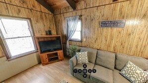 L’intérieur chaleureux d’un chalet, avec un revêtement mural en bois, un canapé, un téléviseur posé sur un meuble en bois et un panneau accroché au mur.