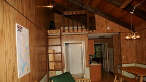 Un intérieur en bois avec un lit en mezzanine, un fauteuil vert, une table en bois et une carte accrochée au mur.