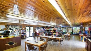 A restaurant with wooden ceiling and walls, tables and chairs, and shelves stocked with various items. - Natchez Trace RV Campground (Hohenwald)