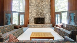 A spacious living room with a stone fireplace, two sofas, a coffee table, and large windows with curtains. - Natchez Trace RV Campground (Hohenwald)