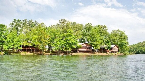 A lakeside property with several wooden cabins surrounded by lush greenery. - Natchez Trace RV Campground (Hohenwald)