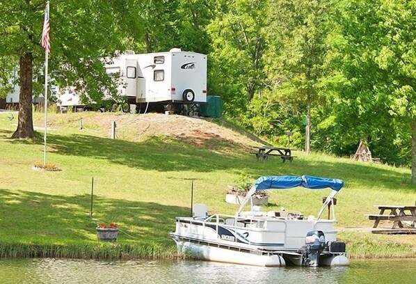 A boat docked at a calm lake with a trailer and RV in the background.