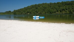 A sandy beach with a clear view of a lake and a forested hill in the background. - Natchez Trace RV Campground (Hohenwald)