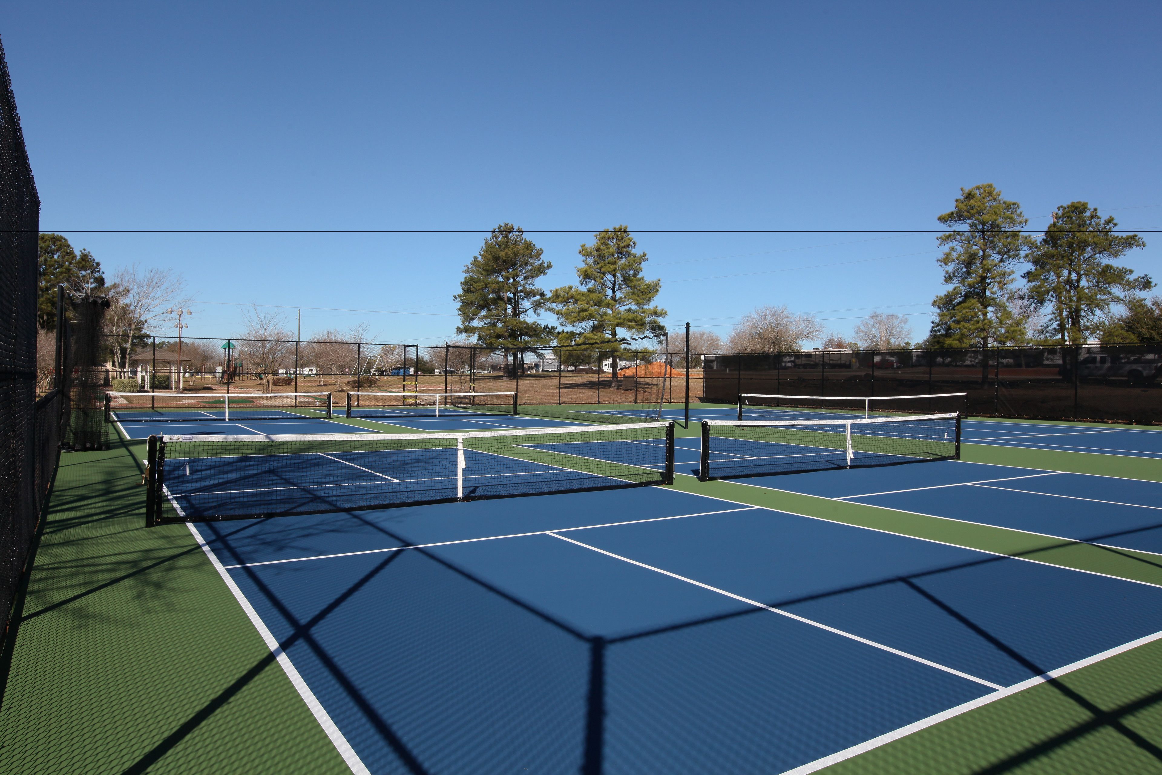 Una cancha de tenis al aire libre con varias canchas, una cerca y árboles al fondo.