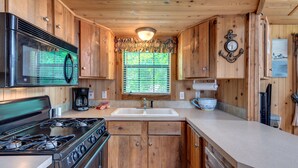 A wooden cabin kitchen with a gas stove, stainless steel microwave, and a sink. - Lake Conroe RV & Camping Resort (Willis)