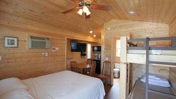 A wooden cabin room with a bed, a desk, a chair, a bunk bed, and a ceiling fan.