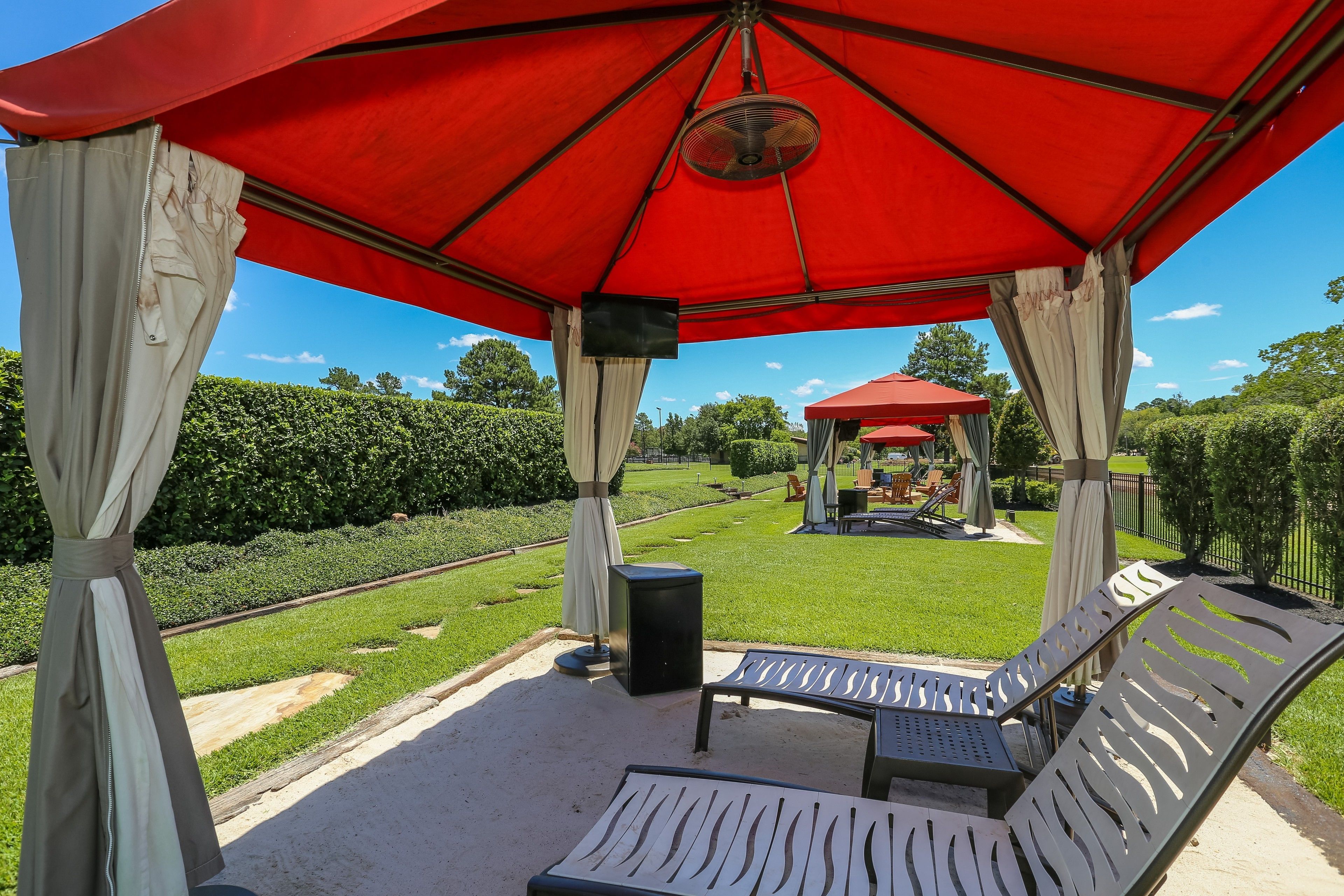 A covered outdoor seating area with a red canopy, white curtains, and a speaker.
