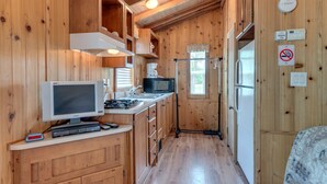 A compact kitchen with wooden walls, a built-in stove, a microwave, and a refrigerator. - Lake Conroe RV & Camping Resort (Willis)