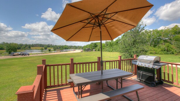 A deck with a picnic table, grill, and umbrella. - Lake Conroe RV & Camping Resort (Willis)