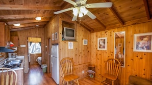 A cabin interior with wooden walls, a ceiling fan, a kitchenette, two wooden chairs, and a couch. - Lake Whitney RV Campground (Whitney)
