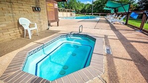 A hot tub area with a brick wall, a white plastic chair, and lounge chairs under a shaded area. - Lake Whitney RV Campground (Whitney)