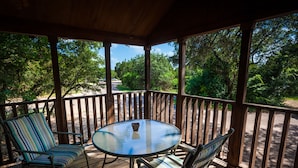 A wooden deck with a glass table and striped chairs, overlooking a road and greenery. - Lake Whitney RV Campground (Whitney)