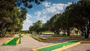 A miniature golf course with multiple green and yellow holes, surrounded by trees and a clear sky. - Lake Whitney RV Campground (Whitney)