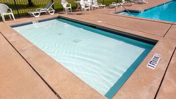 A rectangular pool with a tiled edge, surrounded by lounge chairs and a small table.