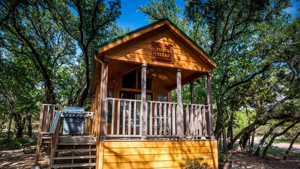A wooden cabin with a sign reading "Fiesta Texas" and a barbecue grill outside. - Lake Whitney RV Campground (Whitney)