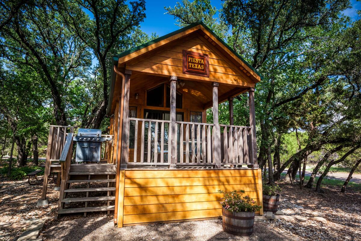 A wooden cabin with a sign reading "Fiesta Texas" and a barbecue grill outside.