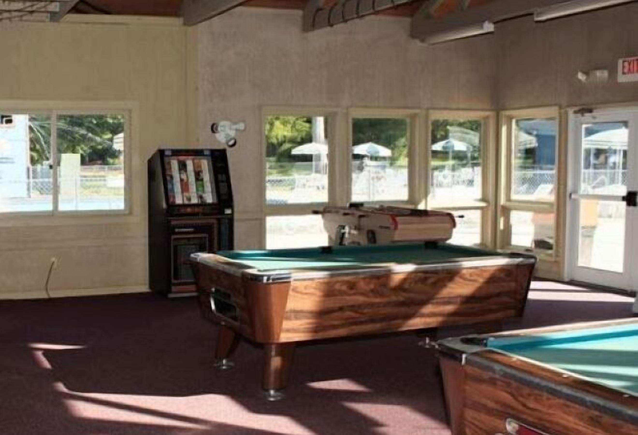A pool table in a room with large windows and a pool table in the background.