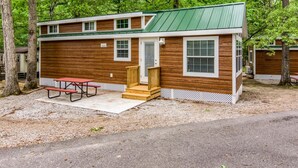 A small, single-story cabin with a green roof, wooden siding, and a front porch. - Williamsburg RV & Camping Resort (Williamsburg)