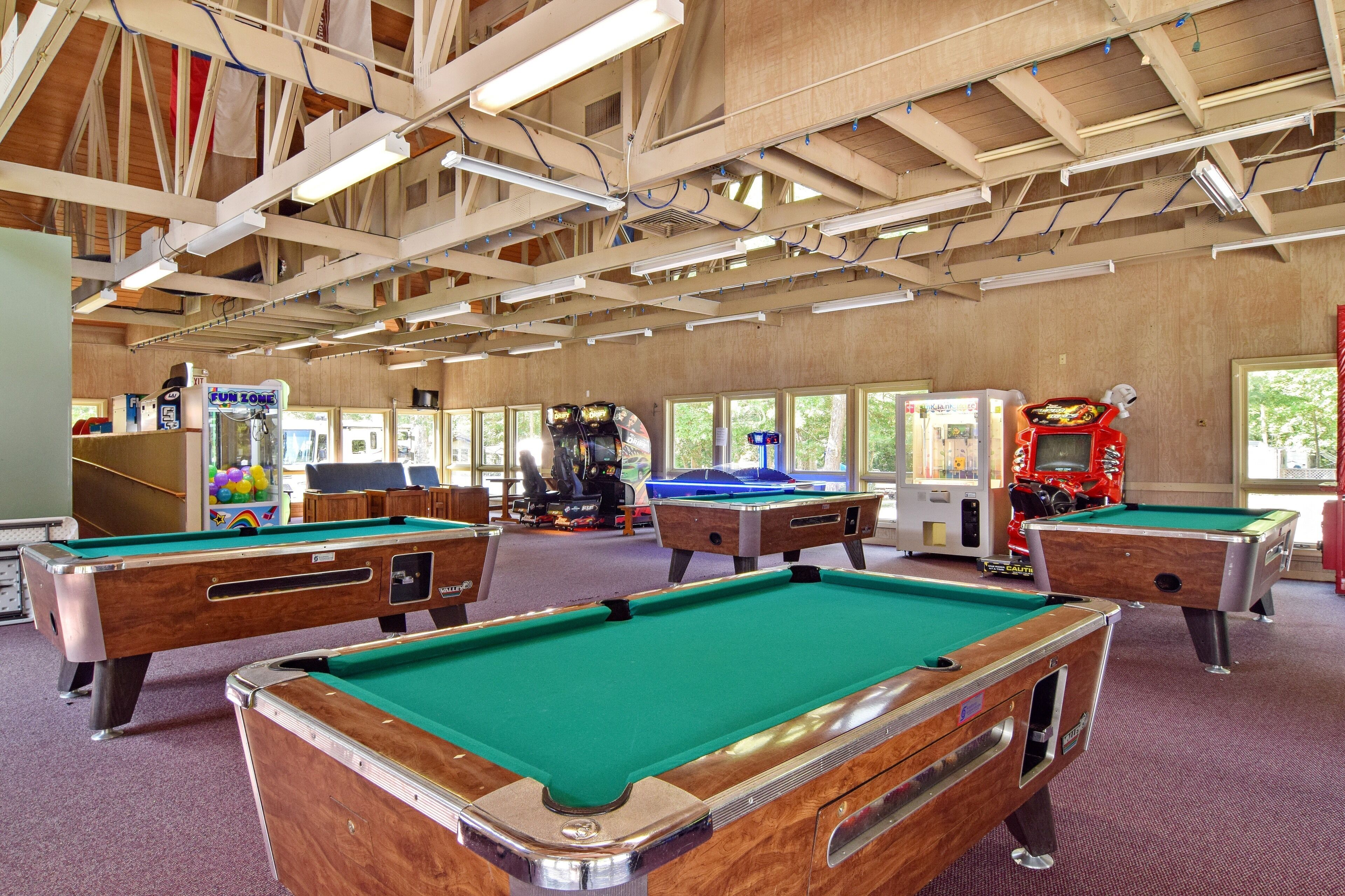 A pool hall with multiple pool tables, arcade games, and a wooden ceiling structure.