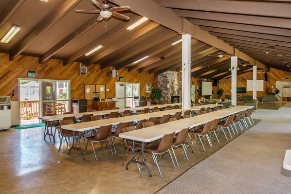 A spacious room with long tables and chairs, wooden walls, and a stone accent wall.