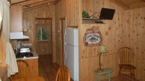 A wooden cabin interior with a kitchen area, a dining table, chairs, a refrigerator, a wall-mounted television, and a Christmas tree. - Chehalis RV & Camping Resort (Chehalis)