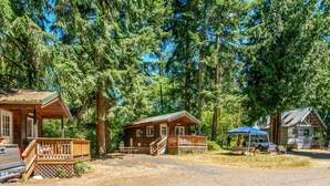 A rustic cabin-style lodging area with multiple cabins, a covered picnic table, and a Chevrolet pickup truck parked nearby. - Chehalis RV & Camping Resort (Chehalis)