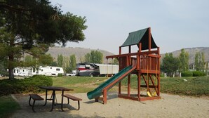 A playground with a slide and swings, a picnic table, and RVs in the background.