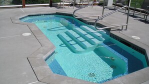 A rectangular swimming pool with a tiled edge, a metal ladder, and a few lounge chairs.