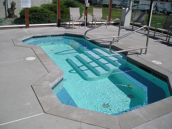 A rectangular swimming pool with a tiled edge, a metal ladder, and a few lounge chairs.