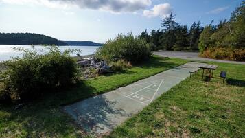 A grassy area with a shuffleboard court, a small table, and a bench near a body of water.