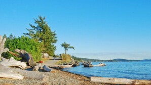 A coastal landscape with a rocky shoreline, trees, and a clear blue sky. - La Conner RV & Camping Resort (La Conner)