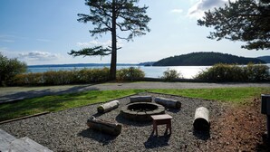 A campsite with a fire pit, logs, and a bench. - La Conner RV & Camping Resort (La Conner)