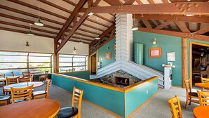 A restaurant with wooden tables and chairs, a stone fireplace, and a view through large windows. - La Conner RV & Camping Resort (La Conner)
