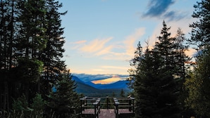 A wooden pathway leading to a viewing platform surrounded by tall trees, overlooking a mountainous landscape.