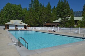 A swimming pool with a white fence, lounge chairs, and a building with a green roof in the background. - Leavenworth RV Campground (Leavenworth)