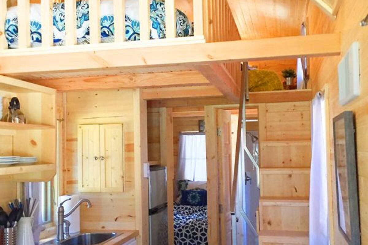 Una cabaña de madera pequeña con una zona de cocina, un comedor y un dormitorio con colcha estampada.