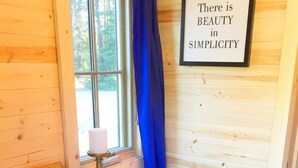 A wooden cabin interior with a dining table set for two, a framed quote on the wall, and a window with a view of trees.