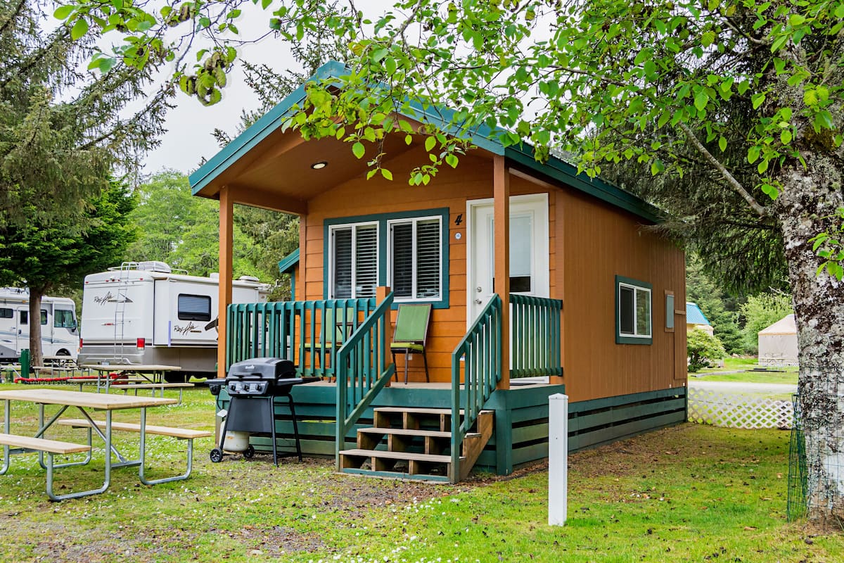 A small wooden cabin with a porch, a grill, and picnic tables.