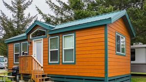 A small wooden cabin with a porch and steps, surrounded by grass and trees. - Long Beach RV & Camping Resort (Ilwaco)